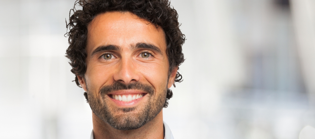 smiling portrait man a man with dark, curly hair and smooth skin smiles brightly