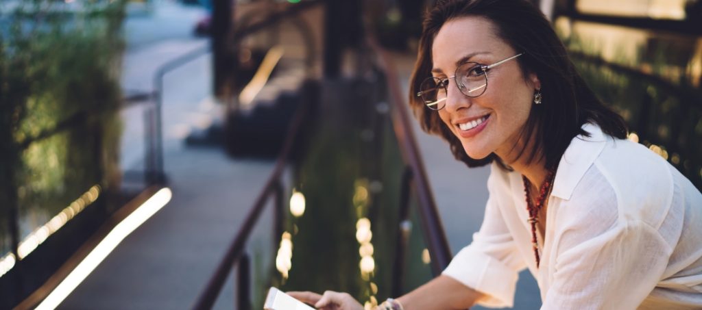 a slim woman in her 30s leans over a handrail smiling