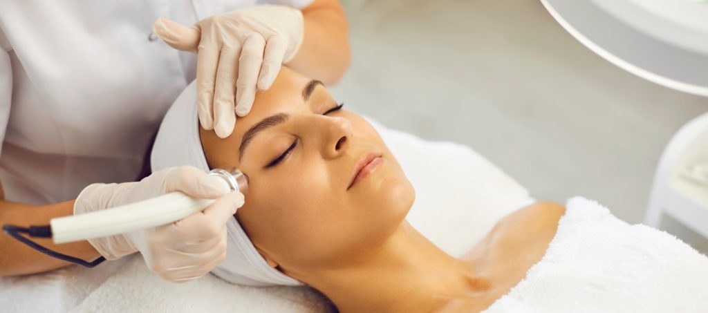 Relaxed young woman with eyes closed getting procedure of vacuum facial cleaning from cosmetologist in gloves in beauty spa salon. Facial treatment, skincare